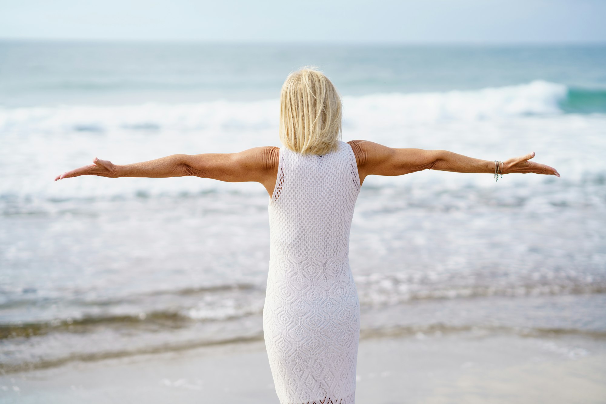 Anonymous mature woman with outstretched arms on seashore