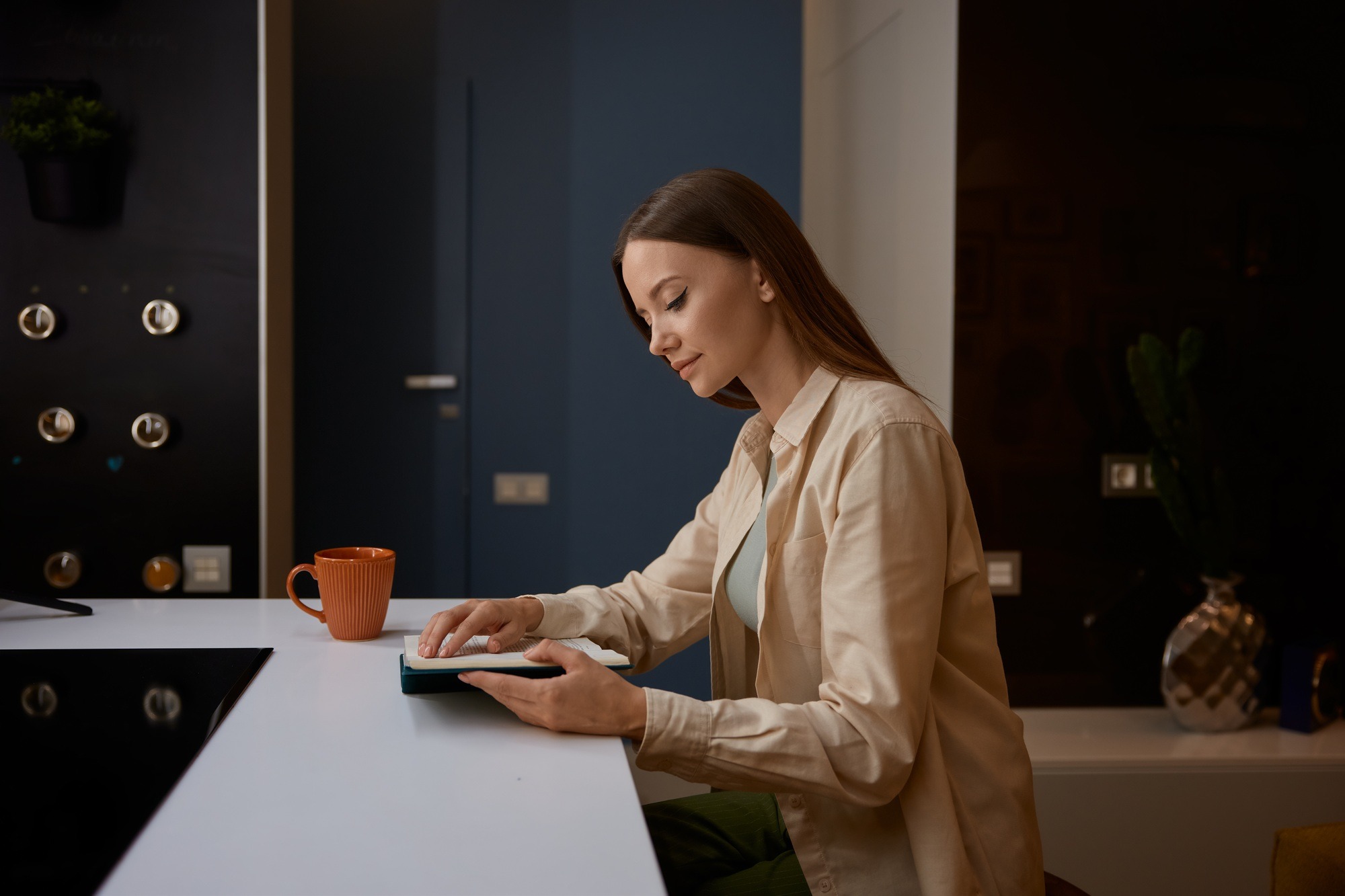 Single young charming woman reading book at home kitchen